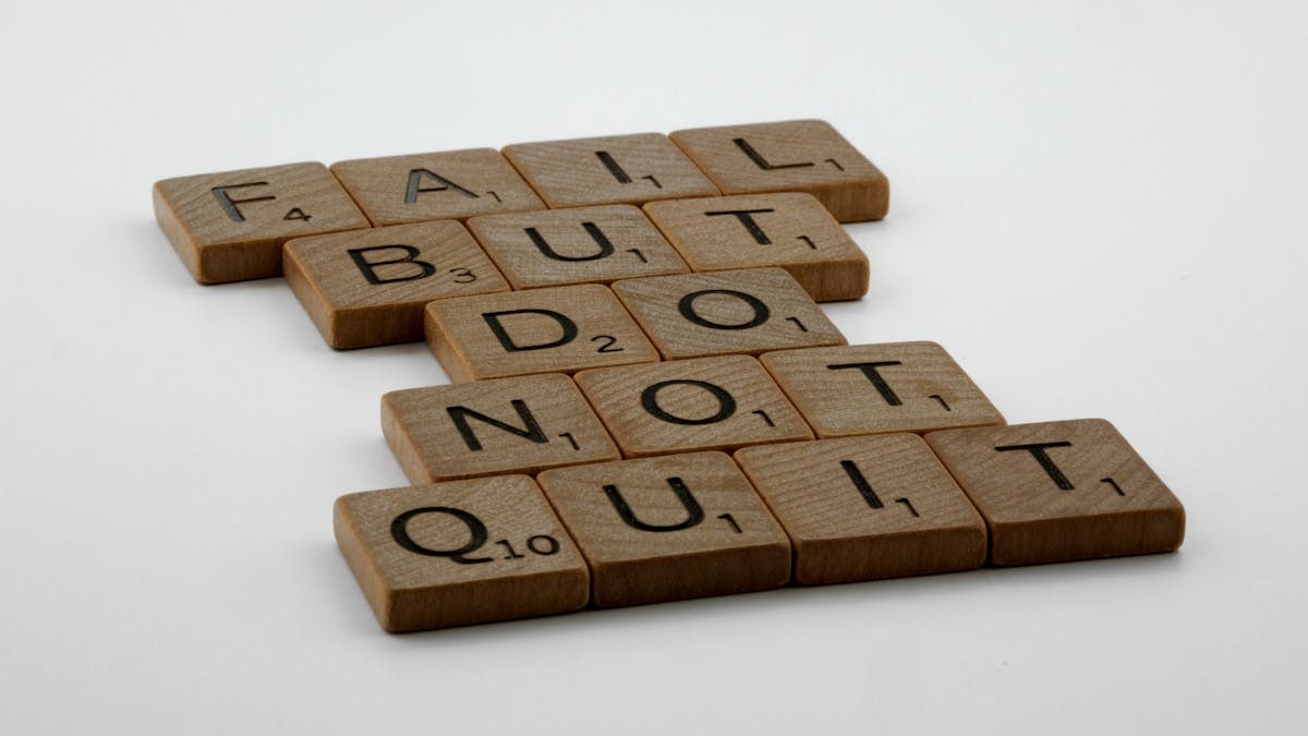Wooden Scrabble tiles arranged to spell 'Fail but do not quit,' inspiring determination.